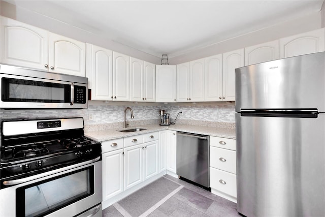 kitchen featuring appliances with stainless steel finishes, a sink, tasteful backsplash, white cabinetry, and light tile patterned floors
