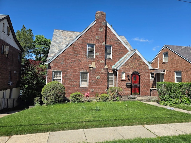 tudor home featuring a front yard, brick siding, and a chimney