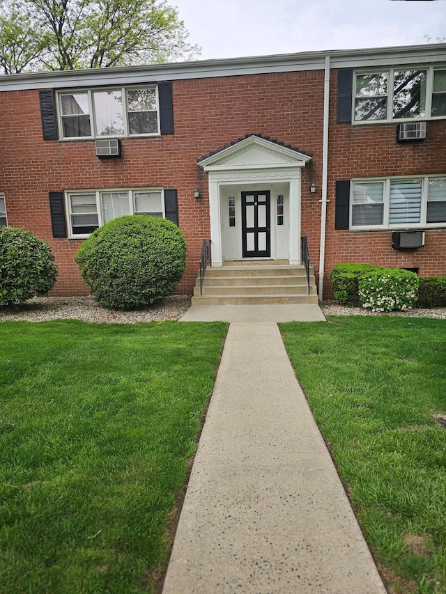 view of front of property with a front yard, brick siding, and a wall mounted AC