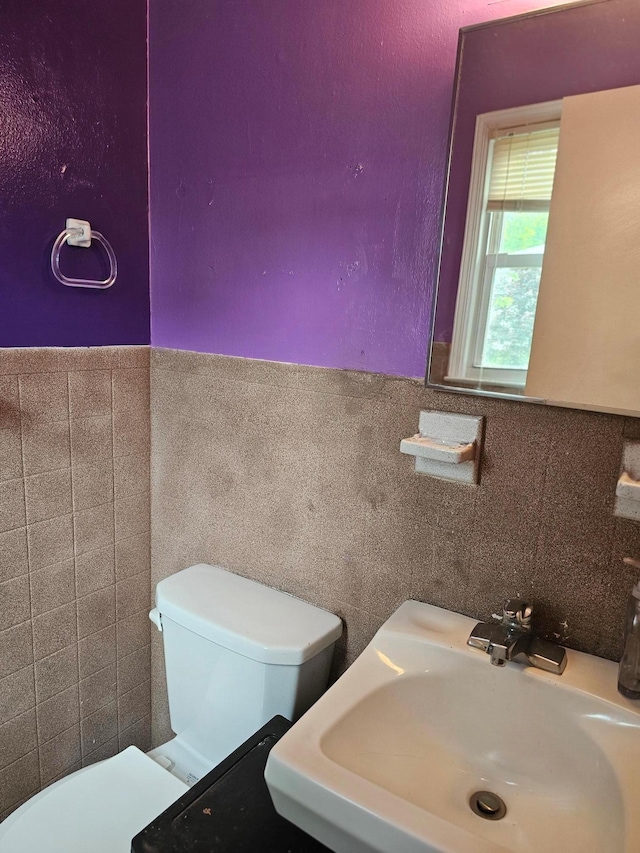 half bathroom with a sink, toilet, tile walls, and a wainscoted wall
