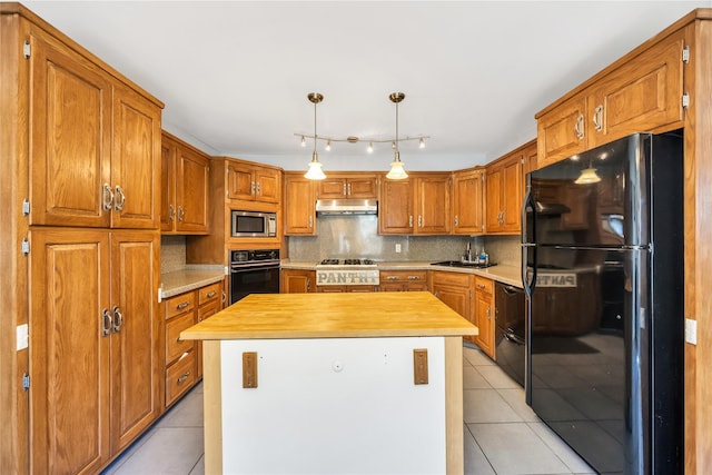kitchen with black appliances, under cabinet range hood, light tile patterned floors, and butcher block counters