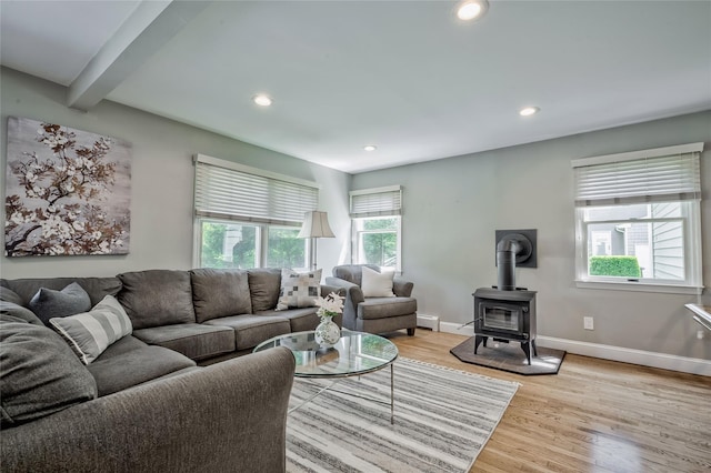 living area featuring light wood-style flooring, a wood stove, recessed lighting, beamed ceiling, and baseboards