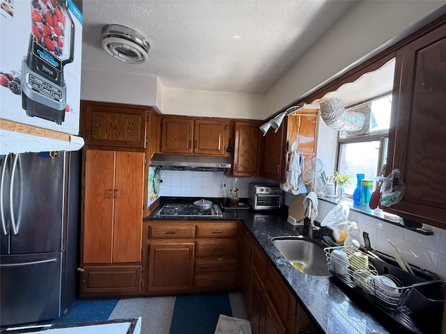 kitchen featuring under cabinet range hood, decorative backsplash, a sink, black gas stovetop, and brown cabinets