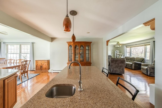 kitchen featuring a sink, a ceiling fan, light wood-style flooring, hanging light fixtures, and light stone counters