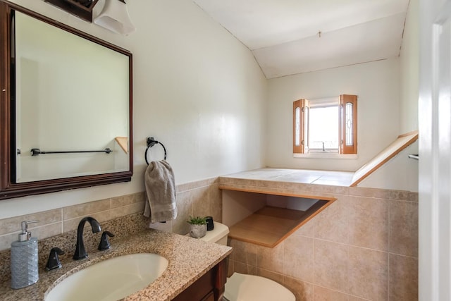 half bathroom with toilet, tile walls, vaulted ceiling, vanity, and wainscoting