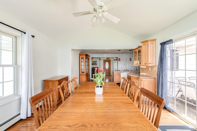 dining area featuring vaulted ceiling, light wood-style flooring, a baseboard radiator, and a ceiling fan