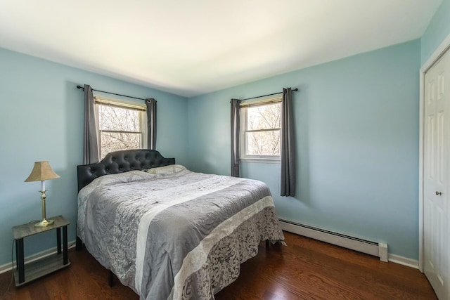 bedroom with a baseboard heating unit, multiple windows, wood finished floors, and baseboards