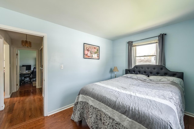 bedroom with wood finished floors, baseboards, a chandelier, and an office area