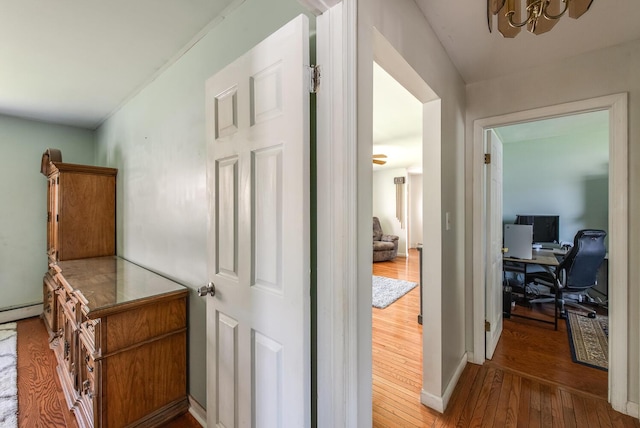 hall featuring an office area, hardwood / wood-style floors, a chandelier, and baseboards