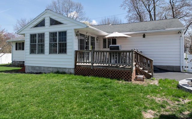 rear view of house with a deck, a yard, and roof with shingles