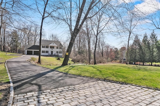 view of property's community featuring a lawn, asphalt driveway, and a detached garage