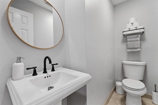 half bath featuring a sink, tile patterned flooring, toilet, and baseboards