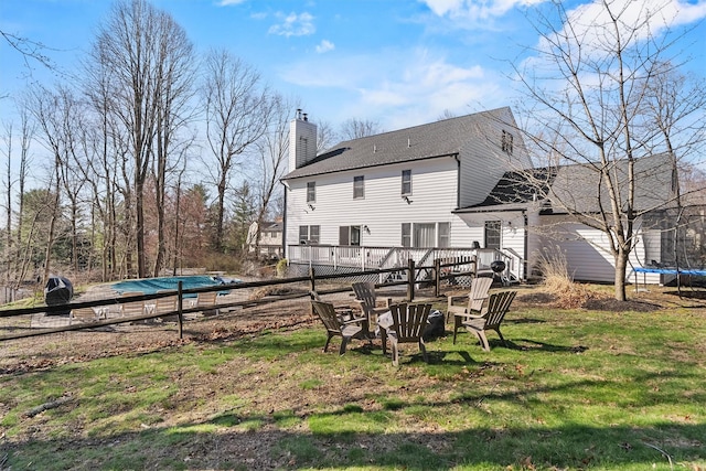 back of house featuring a trampoline, a wooden deck, a lawn, a chimney, and roof with shingles