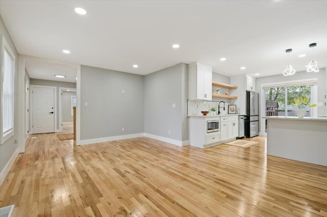 unfurnished living room featuring light wood-style flooring, baseboards, recessed lighting, and a sink