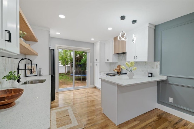 kitchen with white cabinets, a sink, light wood finished floors, a peninsula, and recessed lighting