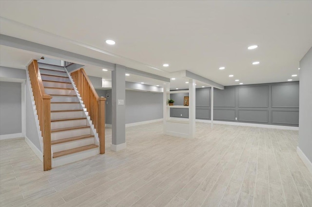 finished below grade area with light wood finished floors, baseboards, stairway, a decorative wall, and recessed lighting