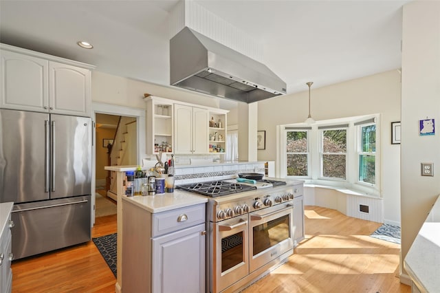 kitchen with high quality appliances, open shelves, light wood-style flooring, wall chimney exhaust hood, and recessed lighting