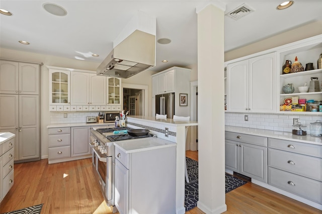 kitchen featuring premium appliances, decorative backsplash, light wood-type flooring, glass insert cabinets, and gray cabinetry