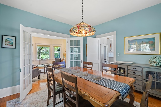 dining space featuring french doors, light wood finished floors, and baseboards