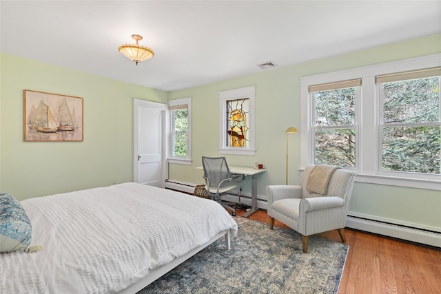 bedroom featuring multiple windows, wood finished floors, and a baseboard radiator