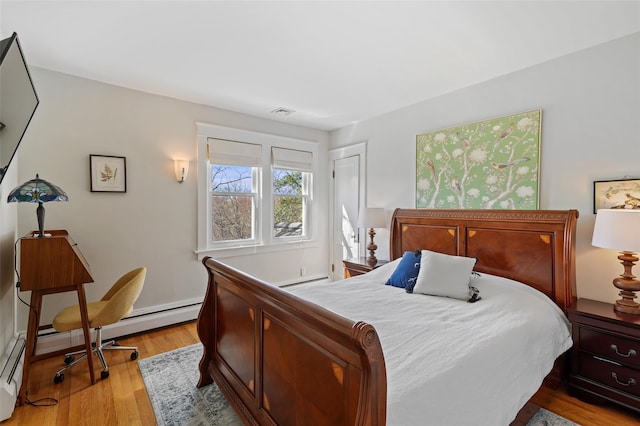 bedroom with light wood finished floors and a baseboard heating unit