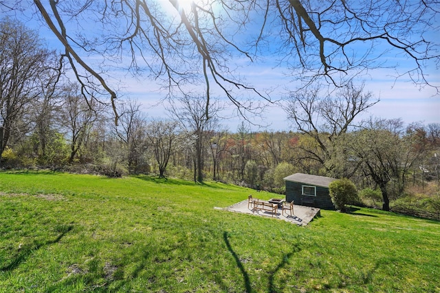 view of grassy yard featuring an outdoor fire pit, an outdoor structure, a wooded view, and a patio