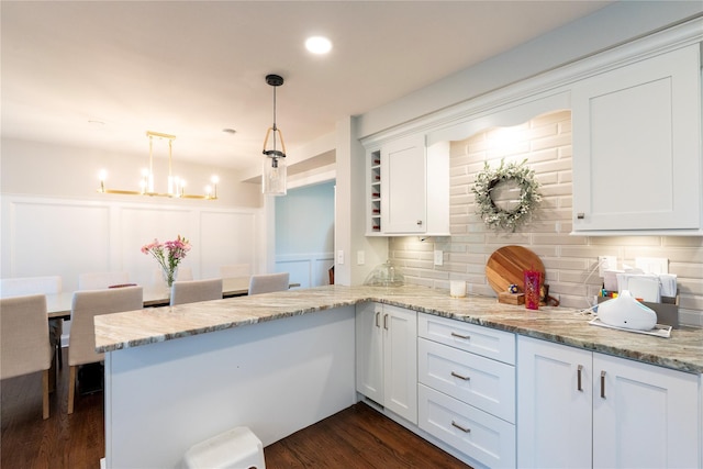 kitchen with a decorative wall, white cabinets, decorative backsplash, a peninsula, and light stone countertops