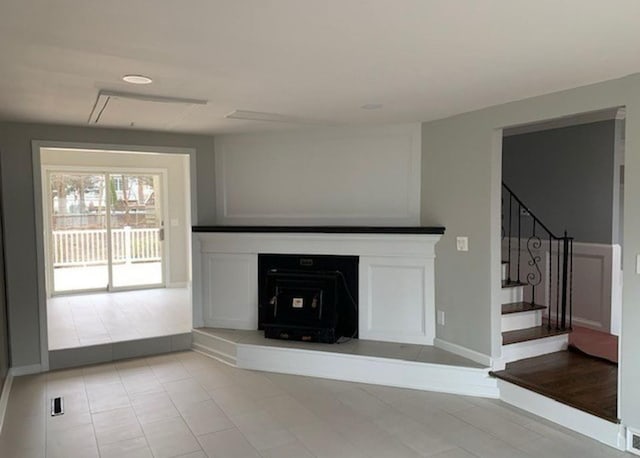 unfurnished living room featuring light tile patterned floors, attic access, baseboards, and stairs