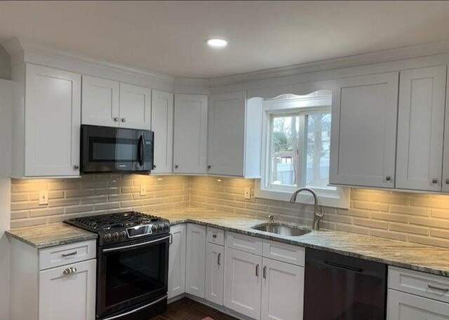 kitchen featuring black appliances, a sink, white cabinetry, light stone counters, and tasteful backsplash
