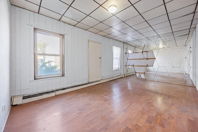 1410 Lincoln Pl, Brooklyn, NY 11213 - empty room featuring healthy amount of natural light, wood finished floors, a baseboard heating unit, and a paneled ceiling