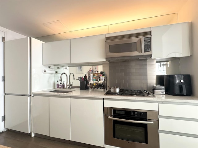 425 E 13th St Unit 1J, New York Manhattan, NY 10009 - kitchen featuring stainless steel appliances, a sink, decorative backsplash, and white cabinets