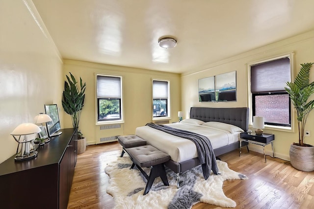 bedroom with radiator heating unit, crown molding, light wood finished floors, and baseboards