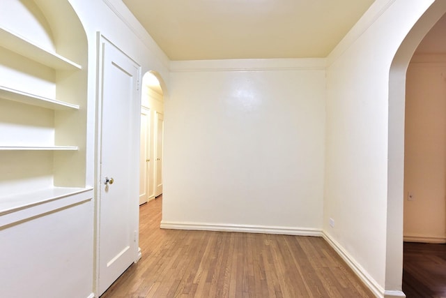 spare room with arched walkways, wood finished floors, and baseboards