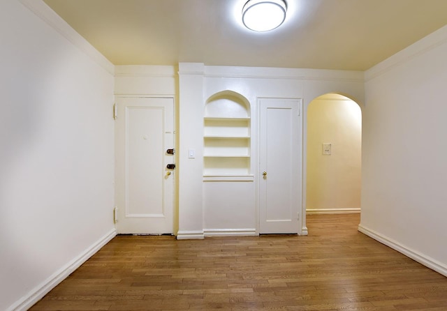 foyer featuring arched walkways, wood finished floors, baseboards, and ornamental molding