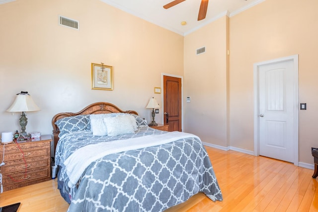 bedroom with a high ceiling, light wood finished floors, ornamental molding, baseboards, and ceiling fan