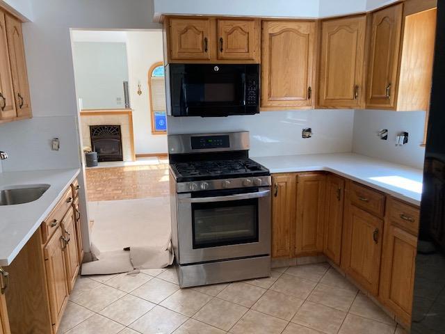 kitchen with stainless steel range with gas stovetop, black microwave, a sink, light countertops, and light tile patterned floors