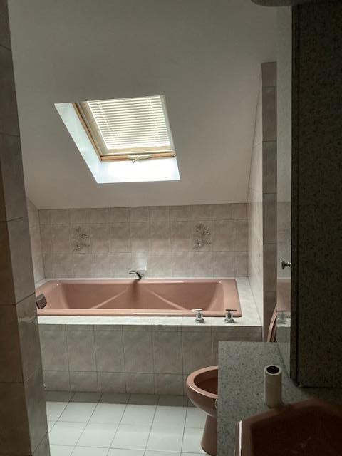 full bathroom featuring tile patterned floors, a garden tub, a skylight, and toilet