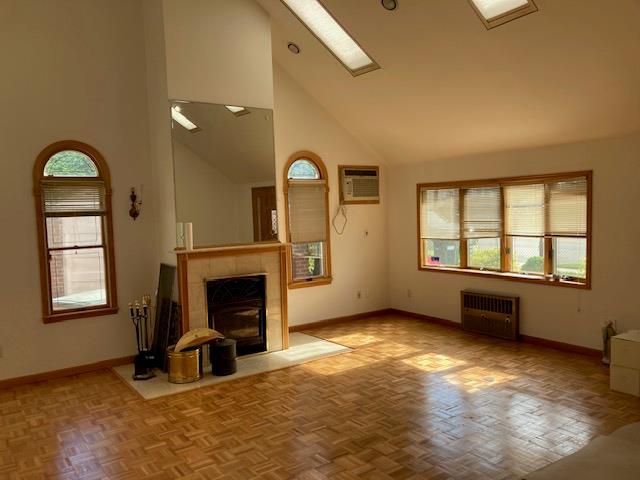 unfurnished living room featuring radiator, a wall mounted air conditioner, baseboards, healthy amount of natural light, and high vaulted ceiling