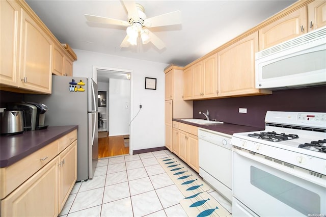kitchen with white appliances, light brown cabinets, a sink, and dark countertops