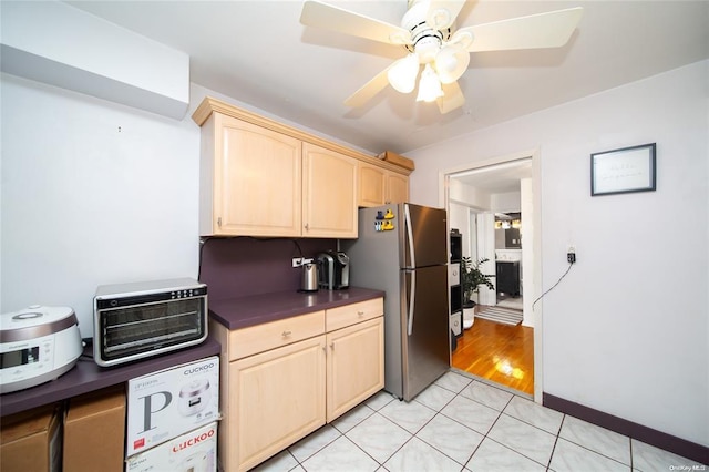 kitchen with freestanding refrigerator, light brown cabinets, dark countertops, and ceiling fan
