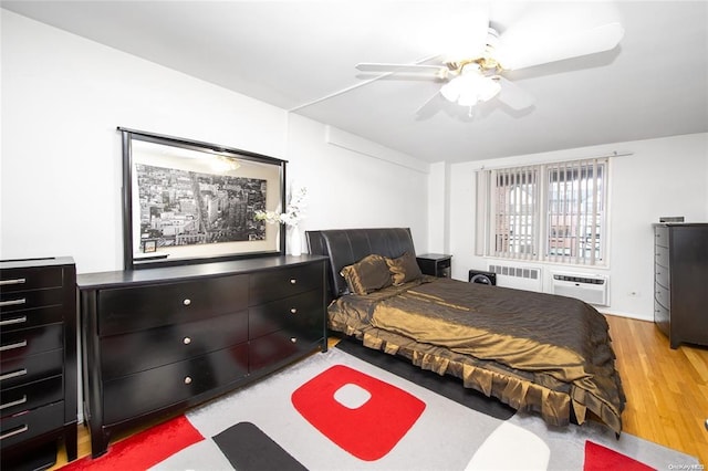 bedroom with radiator, light wood-style flooring, a wall mounted AC, and ceiling fan