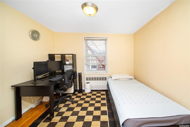 bedroom featuring radiator heating unit, wood finished floors, and a desk
