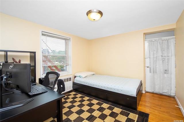 bedroom with radiator, wood finished floors, baseboards, and an office area