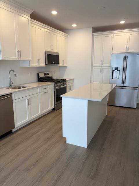 kitchen with appliances with stainless steel finishes, a sink, wood finished floors, white cabinets, and recessed lighting