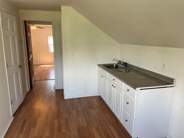 bar featuring dark wood-type flooring, a sink, vaulted ceiling, a ceiling fan, and baseboards
