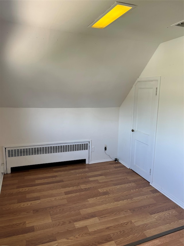 additional living space with vaulted ceiling, a baseboard heating unit, and wood finished floors