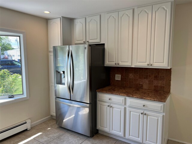 kitchen featuring stainless steel fridge, a baseboard radiator, decorative backsplash, white cabinets, and dark stone counters