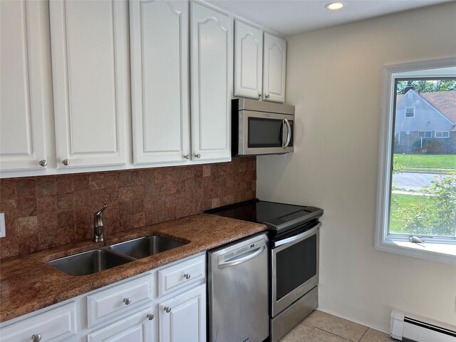 kitchen with appliances with stainless steel finishes, a sink, baseboard heating, decorative backsplash, and white cabinetry