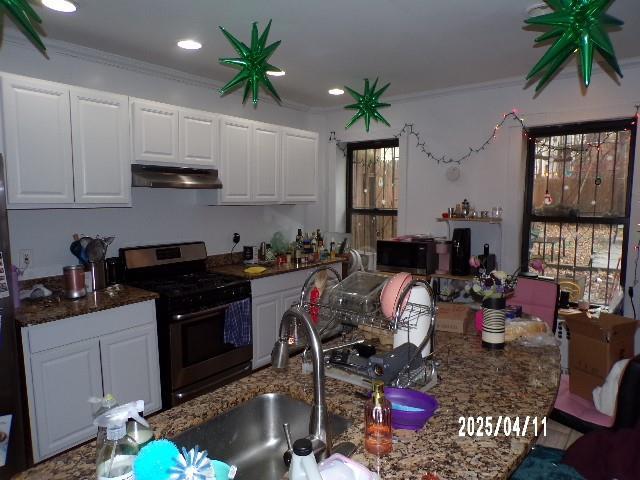 173 Quincy St, Brooklyn, NY 11216 - kitchen with gas range oven, under cabinet range hood, white cabinetry, crown molding, and a sink