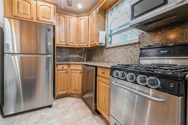 kitchen featuring appliances with stainless steel finishes, a sink, light tile patterned floors, and tasteful backsplash